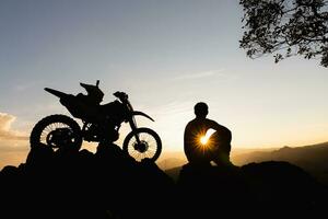 uomo con motocross bicicletta contro bellissimo luci, silhouette di un' uomo con motocross motociclo su superiore di roccia alto montagna a bellissimo tramonto, enduro motociclo viaggio concetto. foto