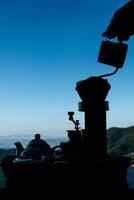 silhouette di il donna fabbricazione gocciolare caffè su il di legno tavolo e un' bellissimo cielo e montagne sfondo foto