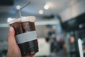 mano Tenere plastica tazza di ghiaccio nero caffè con sfocato sfondo foto