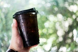 avvicinamento di uomo mani Tenere un' tazza di ghiacciato nero caffè. foto