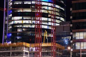 frammento di il bicchiere facciata di un' moderno aziendale edificio a notte. moderno bicchiere ufficio nel città. grande raggiante finestre nel moderno ufficio edifici a notte, nel righe di finestre leggero brilla. foto