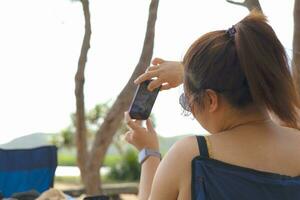 donna indossare buio bicchieri sorridente e assunzione un' foto con smartphone nel il parco.