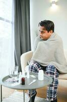 Salute, freddo e persone concetto - malato giovane indiano uomo nel coperta avendo mal di testa o febbre a casa foto