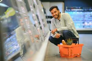 ritratto di contento indiano uomo in piedi nel davanti di il Prodotto contatore nel un' drogheria negozio. uomo acquisto drogheria per casa nel supermercato. foto