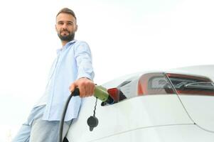 elegante uomo inserti spina in il elettrico auto ricarica presa di corrente foto