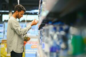 ritratto di contento indiano uomo in piedi nel davanti di il Prodotto contatore nel un' drogheria negozio. uomo acquisto drogheria per casa nel supermercato. foto