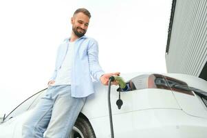 elegante uomo inserti spina in il elettrico auto ricarica presa di corrente foto