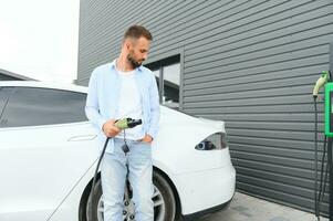 uomo Tenere energia ricarica cavo per elettrico auto nel all'aperto auto parco. e lui S andando per Collegare il auto per il ricarica stazione nel il parcheggio lotto vicino il shopping centro. foto