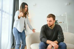 famiglia litigare, uomo e donna seduta su divano a casa. arrabbiato donna urla a sua marito foto