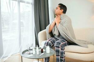 malato giovane indiano uomo sofferenza gola dolore mentre seduta su letto a casa foto