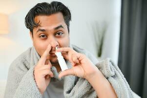 rinite, medicina e assistenza sanitaria concetto - malato indiano uomo nel coperta utilizzando nasale spray a casa foto