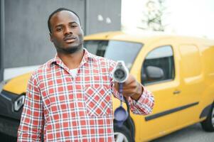 un' africano americano uomo sta Il prossimo per giallo elettrico consegna furgone a elettrico veicolo ricarica stazioni foto