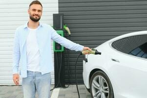 uomo Tenere energia ricarica cavo per elettrico auto nel all'aperto auto parco. e lui S andando per Collegare il auto per il ricarica stazione nel il parcheggio lotto vicino il shopping centro. foto