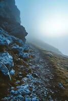ai generato un' tranquillo scena cattura un' nebbioso montagna sentiero con roccioso terreno sotto i piedi, circondato di un' sereno e nebbioso atmosferico fondale foto