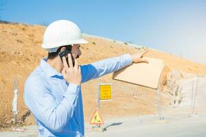 costruzione uomo con bianca casco Lavorando con Telefono. foto