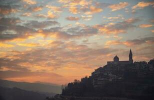 montagnoso Chiesa al di sopra di tramonto cielo sfondo foto