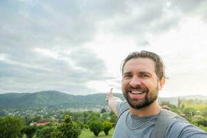 bello uomo assunzione autoscatto foto a Alba su estate vacanza. contento escursionista con zaino sorridente a telecamera fuori. turista a piedi nel il parco.