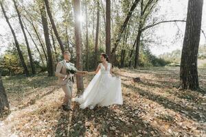 nozze foto nel natura. il sposa e sposo siamo a piedi nel il foresta, Tenere mani e guardare a ogni Altro, il sposa è Tenere sua nozze vestito magnificamente. coppia nel amore. estate luce.