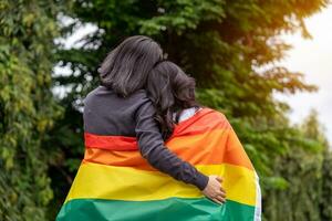 lesbica coppia abbracciare e Tenere lgbt arcobaleno bandiere. omosessualità concetto. foto