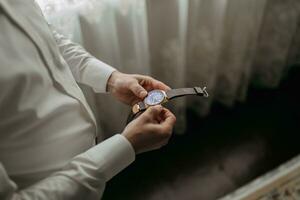 particolari. un' uomo nel un' bianca camicia detiene un' orologio con tutti e due mani. moda e stile. attività commerciale. Uomini stile foto