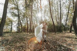 ritratto di contento sposa e sposo nel il foresta. il sposo detiene il sposa nel il suo braccia, danza con suo. un' lungo velo nel il aria. un' raggio di il sole nel il foto. largo angolo foto