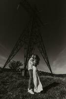 elegante modello coppia nel il montagne nel estate. un' giovane ragazzo e ragazza nel un' bianca seta vestito siamo in piedi vicino grande strutture di energia Linee. nero e bianca contrasto foto