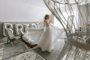 bellissimo Riccio capelli castani sposa nel un' bianca vestito pose per un' fotografo, girando il camera nel un' bellissimo vestito con maniche. nozze fotografia, avvicinamento ritratto, elegante acconciatura. foto