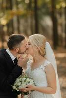 il sposa e sposo contro il sfondo di un' fiaba nebbia nel il foresta, lui baci sua su il guancia. il raggi di il sole rompere attraverso il Fumo, un' fiaba nozze. foto