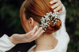 un' bellissimo giovane dai capelli rossi sposa è preparazione per sua nozze. fiori nel capelli. acconciatura con gypsophila foto