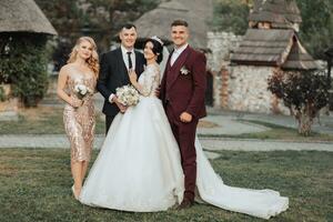 davanti Visualizza di Novelli sposi a piedi mano nel mano tra gli amici. ragazze nel d'oro vestiti hold mazzi di fiori, il sposa nel un' voluminoso vestire, il sposo e il suo amici nel abiti. nozze nel natura foto