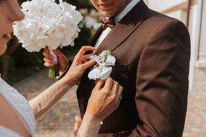 sposa si aggrappa per il giacca di il quello dello sposo boutonniere di fresco fiori foto