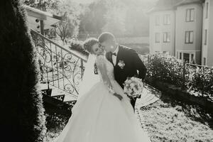 nero e bianca foto. un' sposo nel un' nero completo da uomo e un' bionda sposa camminare Tenere mani vicino un' pietra parete sotto un' albero. un' bianca, lungo velo nel il aria. foto sessione nel natura. bellissimo capelli