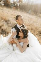 ritratto di un' elegante sposo con un' sposa su un' sfondo di autunno asciutto erba. il concetto di un' rurale nozze nel il montagne, contento boemo Novelli sposi. il sposa e sposo siamo dire bugie su il erba foto