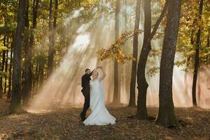 il sposa e sposo siamo danza contro il sfondo di un' fiaba nebbia nel il foresta. il raggi di il sole rompere attraverso il Fumo, un' fiaba nozze foto