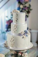 un' bianca nozze torta, decorato con fiori e oro, sta su un' bicchiere In piedi. fresco fiori a il nozze. dolci foto