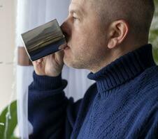 ritratto di il medio anziano uomo con grigio capelli, indossare caldo, buio blu maglione, potabile caffè. persone foto