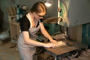 femmina falegname indossare protettivo sicurezza bicchieri e utilizzando elettrico opera su un' Di legno. artista o mobilia progettista Lavorando su un' Prodotto idea nel un' officina. foto