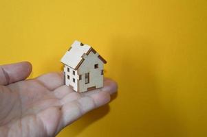 piccola casa di legno in mano d'uomo su sfondo giallo