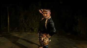un indonesiano uomo balli con determinazione e abilità mentre indossare un' nero costume su palcoscenico foto