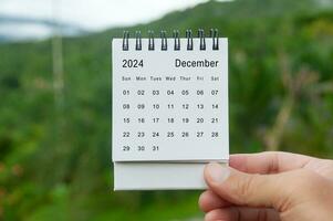 mano Tenere dicembre 2024 bianca calendario con natura sfondo. vacanza e calendario concetto foto