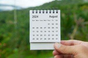 mano Tenere agosto 2024 bianca calendario con natura sfondo. vacanza e calendario concetto foto