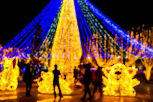 avvicinamento sfocato e bokeh di Natale vacanza illuminazione con silhouette di persone nel notte tempo sfondo. foto