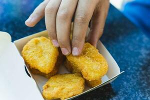 un' del bambino mano prende delizioso d'oro fritte pepite a partire dal un' carta scatola su un' tavolo nel un' bar foto