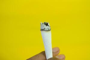 un' uomo mano detiene un' fatto a mano sigaretta su giallo sfondo foto