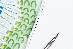 100 banconote in euro con blocco note vuoto e penna su sfondo bianco foto