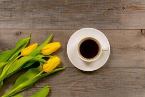tulipani gialli e tazza di caffè su tavola in legno rustico. vista dall'alto con spazio di copia. foto