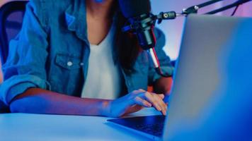 felice asia ragazza host registrare podcast utilizzare microfono indossare cuffie con laptop intervista ospite conversazione per contenuti nel suo studio di casa di notte. concetto di apparecchiature audio. concetto di creatore di contenuti. foto