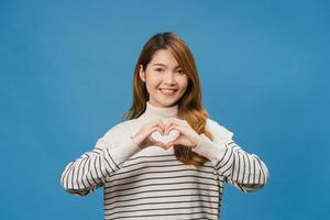 giovane donna asiatica con espressione positiva, mostra il gesto delle mani a forma di cuore, vestita con abiti casual e guardando la telecamera isolata su sfondo blu. felice adorabile donna felice esulta successo. foto