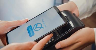 giovane donna asiatica self service usa il telefono cellulare paga senza contatto con la macchina del lettore di carte di credito al bar ristorante. proprietario piccola impresa, tecnologia senza contanti e concetto di trasferimento di denaro. colpo da vicino. foto