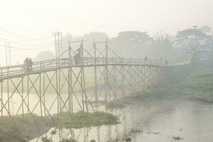 abitanti del villaggio attraversamento su il tradizionale bambù ponte su un' nebbioso mattina nel bangladesh foto